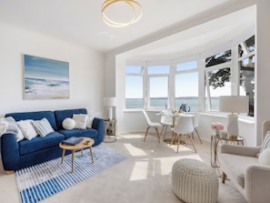 A modern living room with a blue sofa, a coffee table, and a view of the sea through large windows.