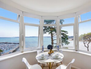 Ruokailutila, jossa on neljälle katettu ruokapöytä, ja suurista ikkunoista avautuu näkymä merelle ja laiturille.