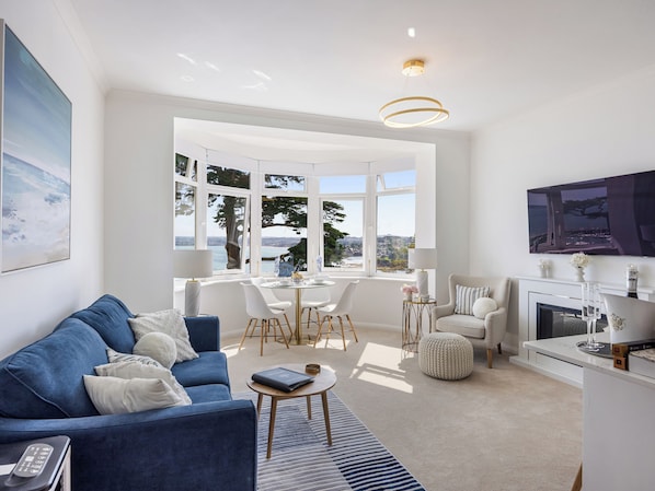 A modern living room with a blue sofa, a dining table, and a fireplace.