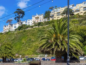 A coastal hillside with residential buildings, palm trees, and parked cars.