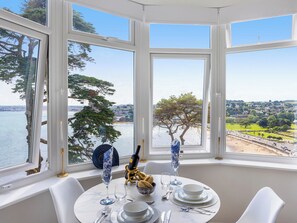 A dining area with a table set for two, large windows offering a view of the sea and a distant landscape.