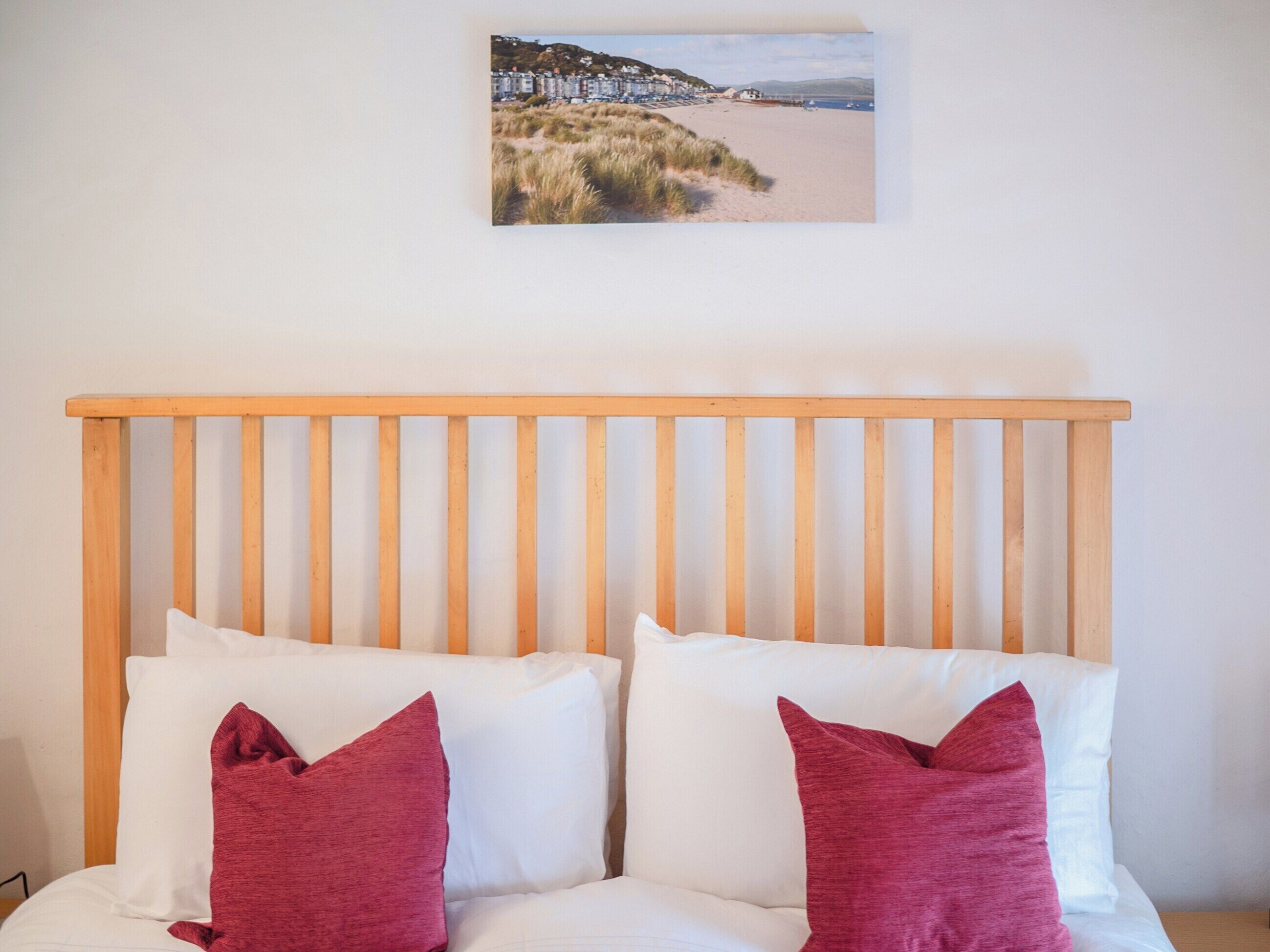 A bed with a wooden headboard, white bedding, and two red pillows.