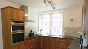 A modern kitchen with wooden cabinets, stainless steel appliances, a window with natural light, and a view of greenery outside. - 3 bedroom accommodation in Corrie, Isle of Arran (Corrie, Isle of Arran)