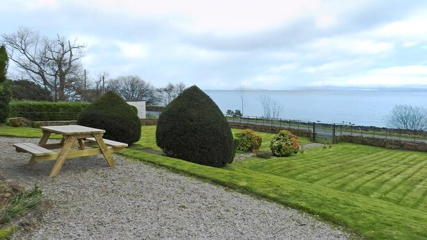 A picnic table and two large bushes in a well-maintained garden with a view of the sea. - 3 bedroom accommodation in Corrie, Isle of Arran (Corrie, Isle of Arran)
