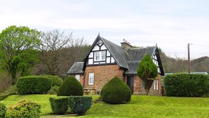 A traditional stone house with a steeply pitched roof, a prominent chimney, and a well-maintained lawn with trimmed hedges. - 3 bedroom accommodation in Corrie, Isle of Arran (Corrie, Isle of Arran)