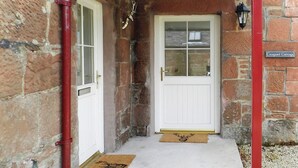 A stone building with a white door, a red gutter, and a doormat with a deer head. - 2 bedroom accommodation in Corrie, Isle of Arran (Corrie, Isle of Arran)
