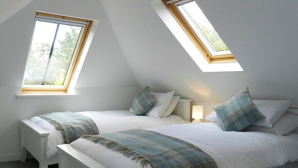 A bedroom with two beds, a skylight, and a bedside table with a lamp. - 2 bedroom accommodation in Corrie, Isle of Arran (Corrie, Isle of Arran)