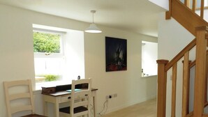A room with a wooden desk, two chairs, a hanging light fixture, and a window with a view of greenery. - 2 bedroom accommodation in Corrie, Isle of Arran (Corrie, Isle of Arran)