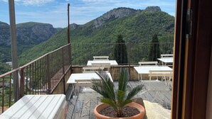 A balcony with a potted plant, outdoor furniture, and a view of a mountainous landscape. - Historic house surrounded by greenery, near outdoor activities and sea (Liguria)