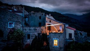 A stone building with a lit window, surrounded by vegetation and a mountainous backdrop. - Historic house surrounded by greenery, near outdoor activities and sea (Liguria)