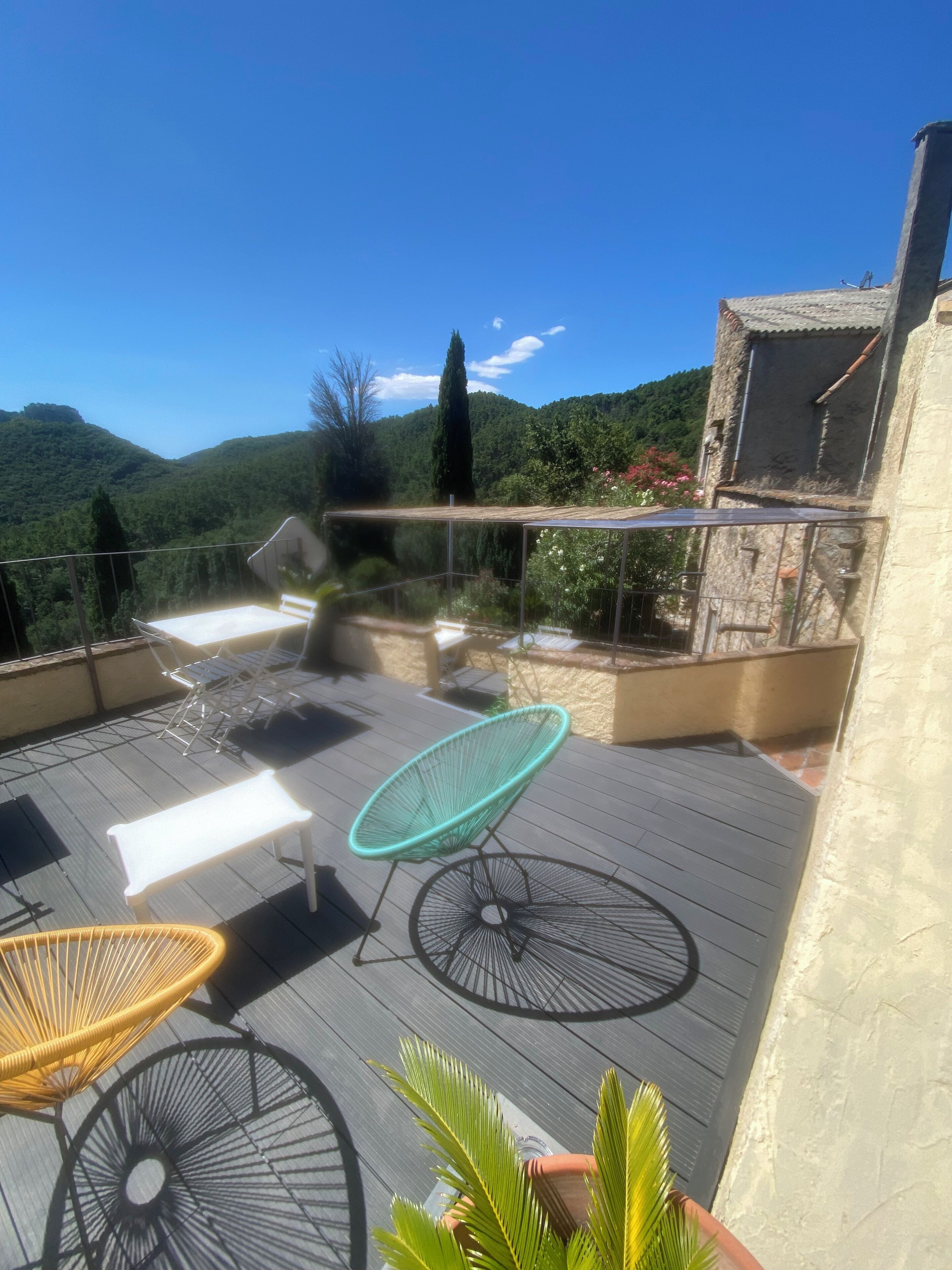 Une terrasse sur le toit, aménagée avec du mobilier d’extérieur, offrant une vue sur un paysage montagneux et donnant sur un bâtiment en pierre.