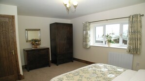 Een slaapkamer met een bed, een dressoir, een kledingkast, een raam met gordijnen en een spiegel aan de muur.