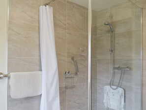Une douche avec une porte en verre, une serviette blanche et un pommeau de douche.