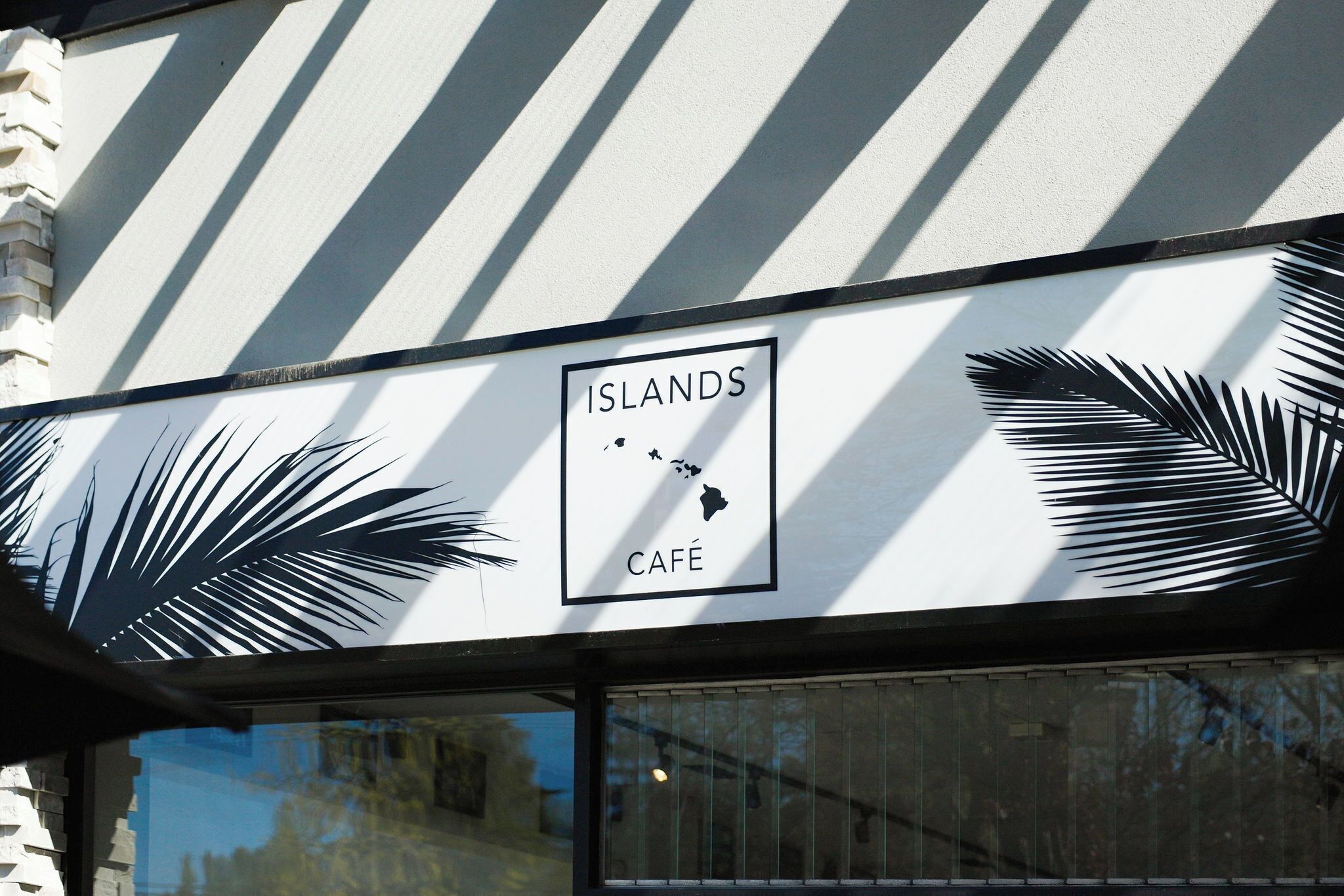 A sign with palm leaves and the words "ISLANDS CAFÉ" on a building facade.