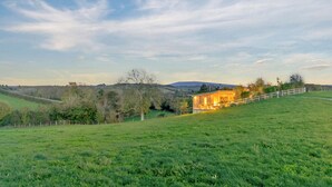Een landelijk landschap met een huis op een heuvel, omringd door groene velden en bomen.