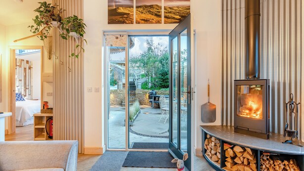 Een gezellige woonkamer met een open haard, een glazen deur naar een terras, en een kleine hond.