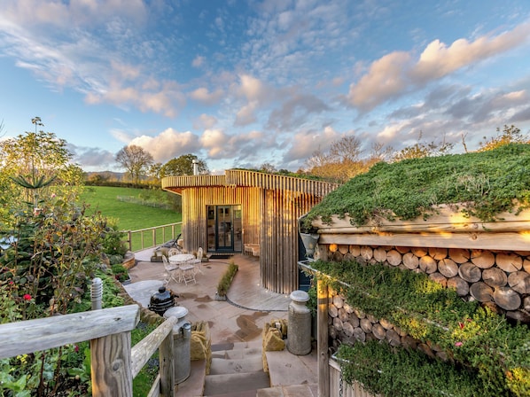 Une structure en bois dotée d’une porte en verre, entourée d’un jardin et d’un mur de pierre.