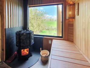 A room with a stone fireplace, a window with a view of greenery, and a wooden bench.