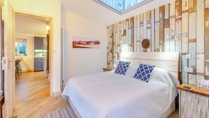 Een slaapkamer met dakraam, een bed met opvallende kussens, een houten hoofdbord en uitzicht op de keuken.