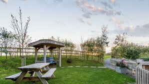 Een picknickplaats met een houten tafel en banken, een prieel en een omheinde tuin.