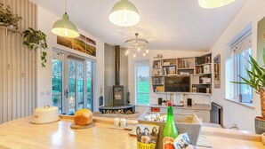 Een moderne keuken met een centraal eiland, hanglampen, een ingebouwde open haard en een groot raam met uitzicht op de omgeving.