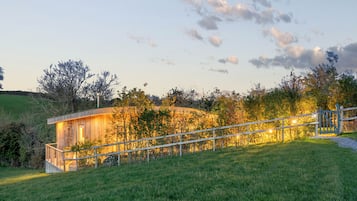 A modern house with a wooden exterior, a staircase leading up to a deck, and a view of the surrounding landscape.