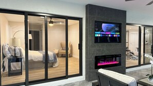 Et moderne hotelværelse med en stor skydedør, der fører til en balkon, et fladskærms-tv på væggen og en indbygget pejs.