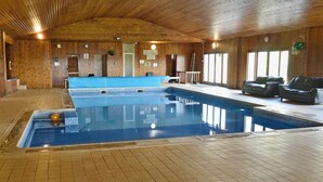 Ein Hallenbad mit gefliestem Boden, Holzwänden und einer Decke mit Holzbalken.