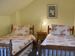 Deux lits simples avec une literie à motifs floraux, une table de chevet avec une lampe et un tableau encadré au mur.