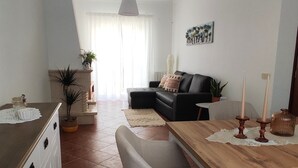A modern living room with a sofa, a dining table, and a kitchen area. - Casa das Rosas- Villa with garden, Charneca da Cotovia (Charneca da Cotovia)