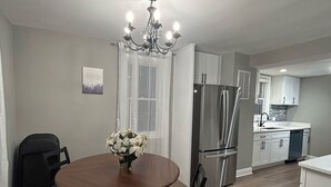Una cocina moderna con armarios blancos, electrodomésticos de acero inoxidable y un comedor con mesa y sillas de madera.