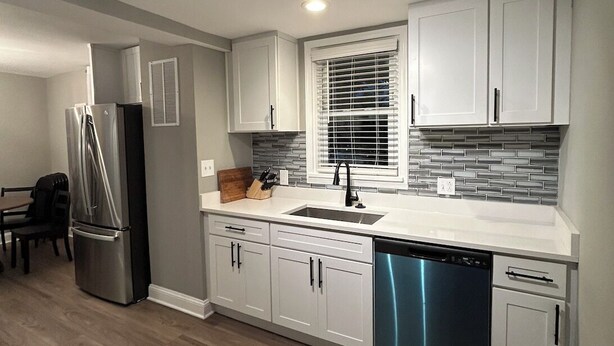 Una cocina moderna con gabinetes blancos, un refrigerador de acero inoxidable, un lavavajillas y una ventana con persianas.