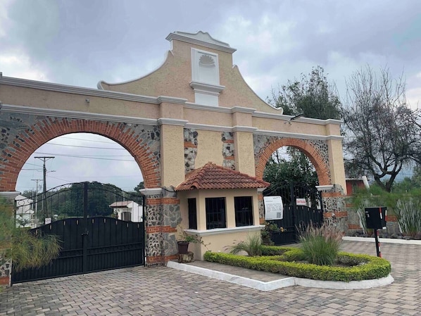 A historic building with a large archway entrance, a gated driveway, and a small garden area.