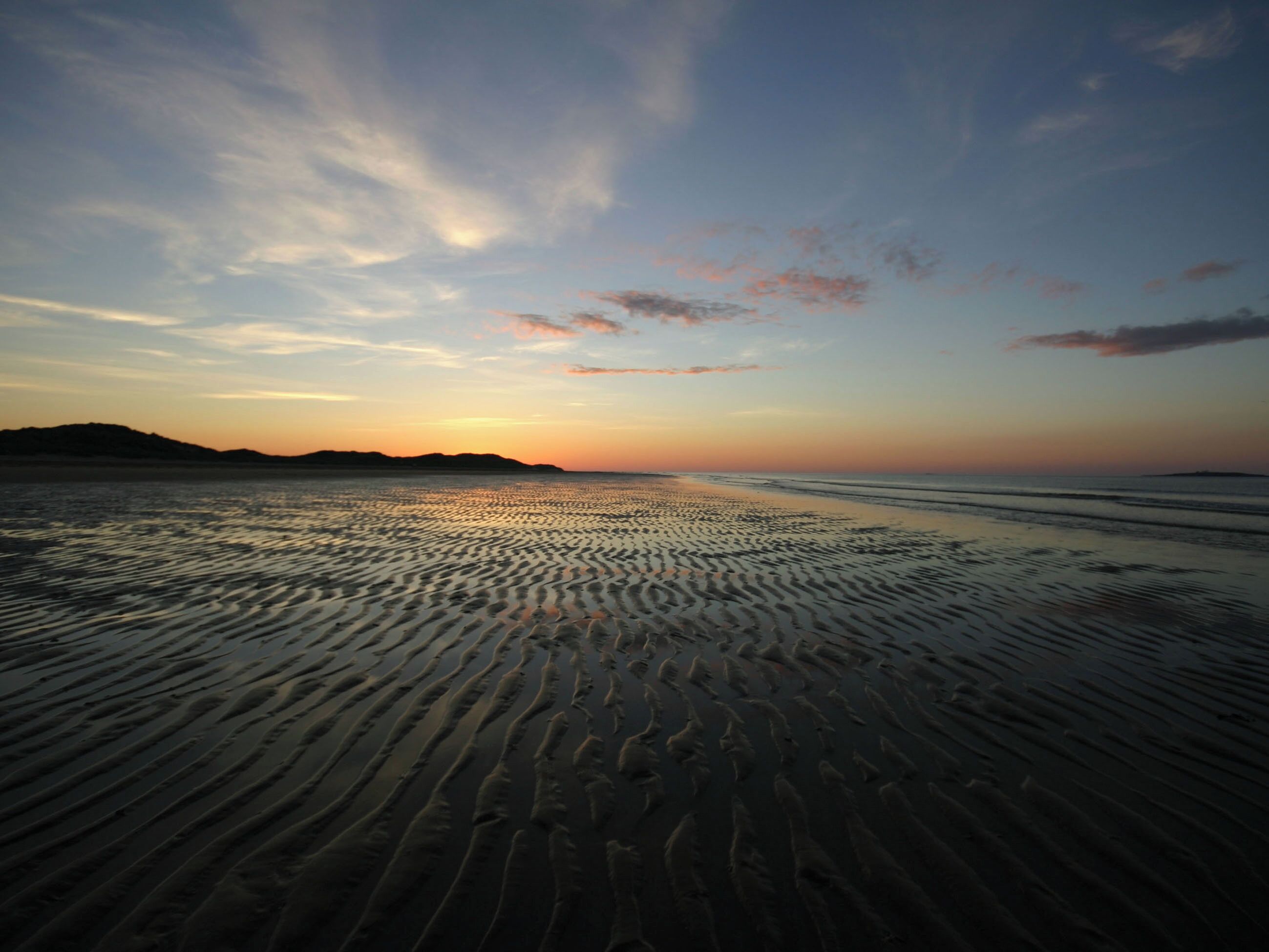 A beach with rippled sand patterns and a sunset in the background.