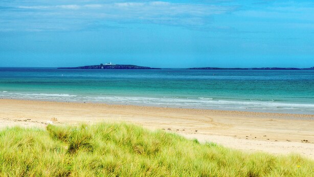 A beach with a lighthouse on a small island in the distance.