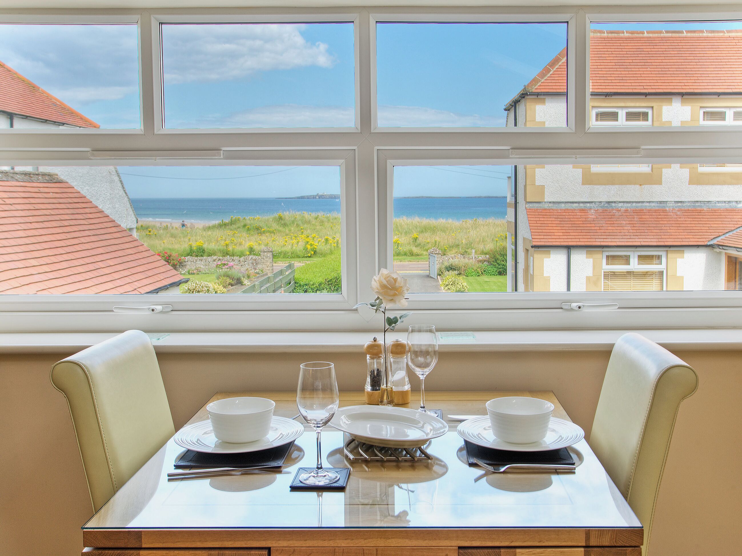 Une table à manger dressée pour deux personnes, avec vue sur la mer par la fenêtre.