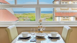 A dining table set for two with a view of the sea through a window.