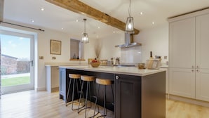 A modern kitchen with a large island, bar stools, pendant lights, and a view to the outside. - Hares Hollow - UK33953 (Llanymynech)