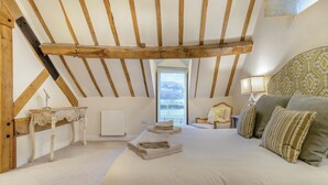 A bedroom with a sloped ceiling, a bed with pillows, a bedside table, a chair, and a window. - Hares Hollow - UK33953 (Llanymynech)