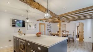 A modern kitchen with a large island, wooden beams, recessed lighting, and a dining area with a wooden table and chairs. - Hares Hollow - UK33953 (Llanymynech)
