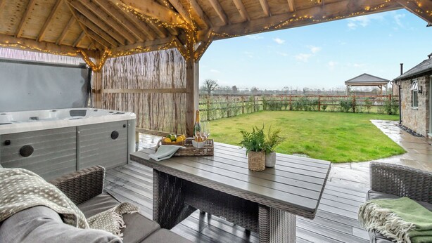 An outdoor patio with a wooden ceiling, string lights, a hot tub, wicker furniture, and a view of a grassy yard. - Hares Hollow - UK33953 (Llanymynech)