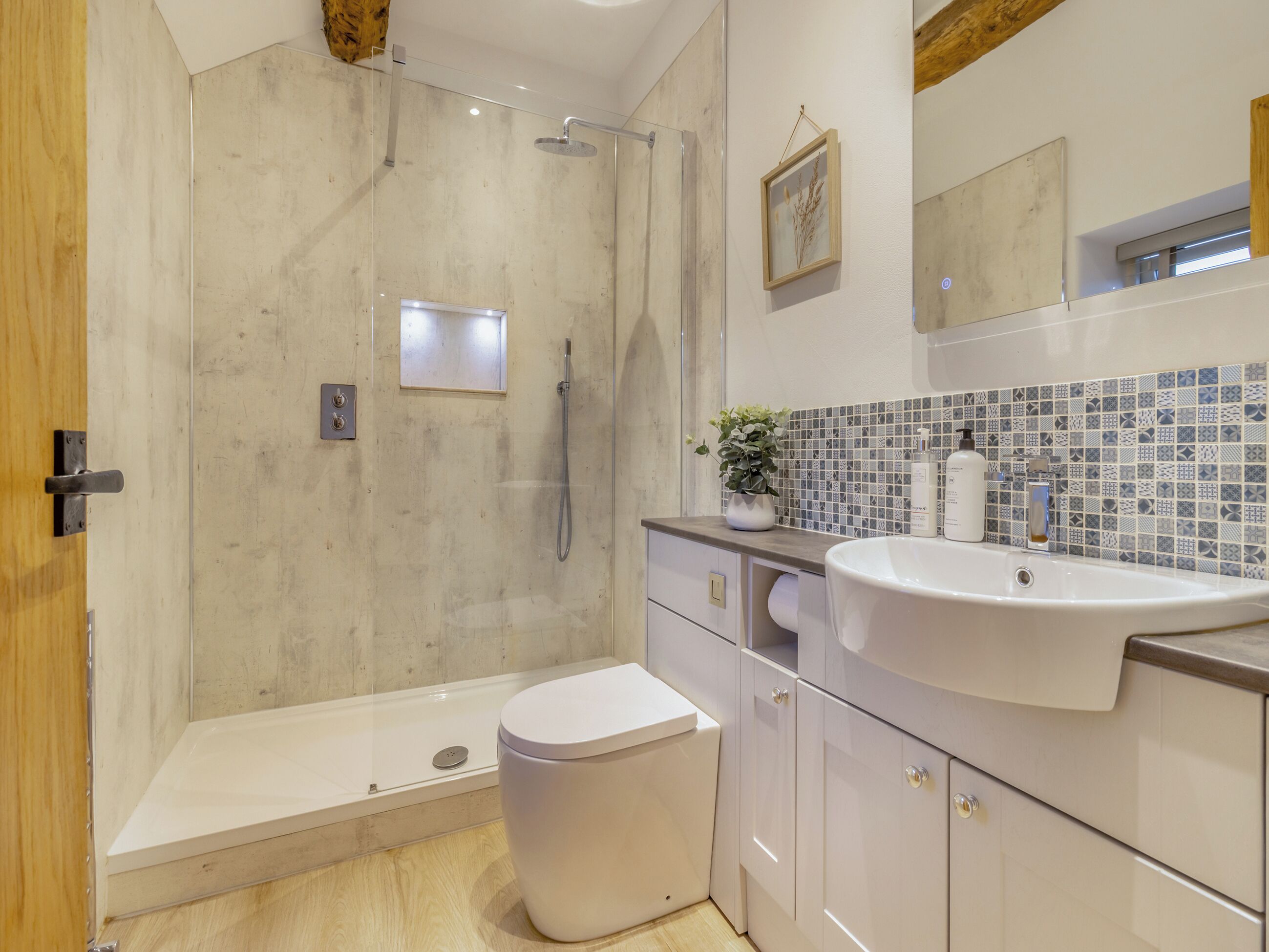 A modern bathroom with a shower, toilet, sink, and tiled backsplash.