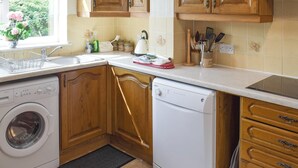 Een keuken met houten kastjes, een wasmachine, een vaatwasser en een raam met uitzicht op een huis en groen.