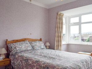 A bedroom with a wooden bed, floral bedding, a bedside table with a lamp, and a window with curtains. - Beautiful location, ideal for families and walkers. (Robin Hood&rsquo;s Bay)