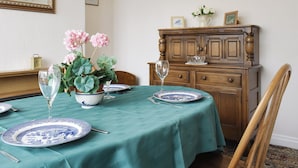 Een eetkamer met een tafel gedekt voor vier personen, met blauwe en witte borden, een groene tafelkleed en roze bloemen in een vaas.
