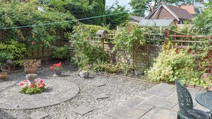 Een tuinpatio met een stenen tafel en een metalen stoel, omringd door grind en potplanten.
