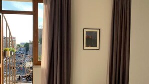 Une chambre moderne dotée d’une grande fenêtre, de rideaux, d’un tableau encadré et d’une petite table avec un banc.