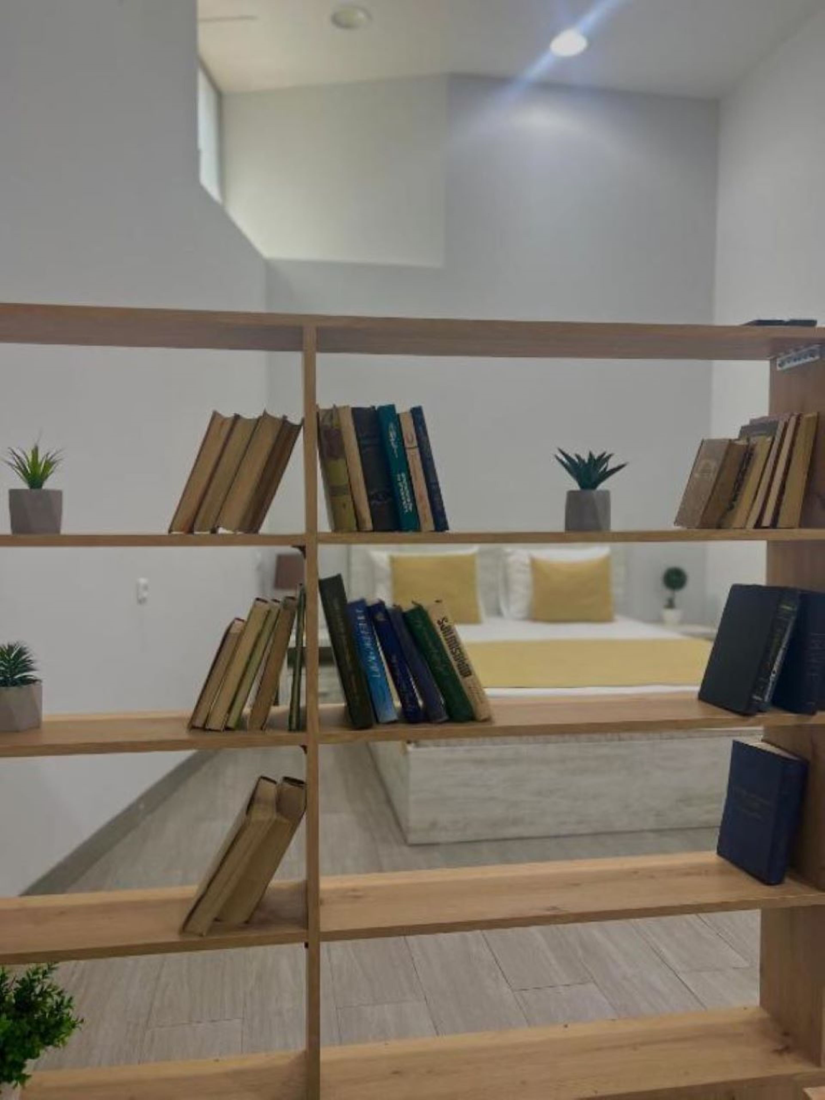 A modern room with a built-in bookshelf, a bed with a yellow pillow, and a small plant on the floor.
