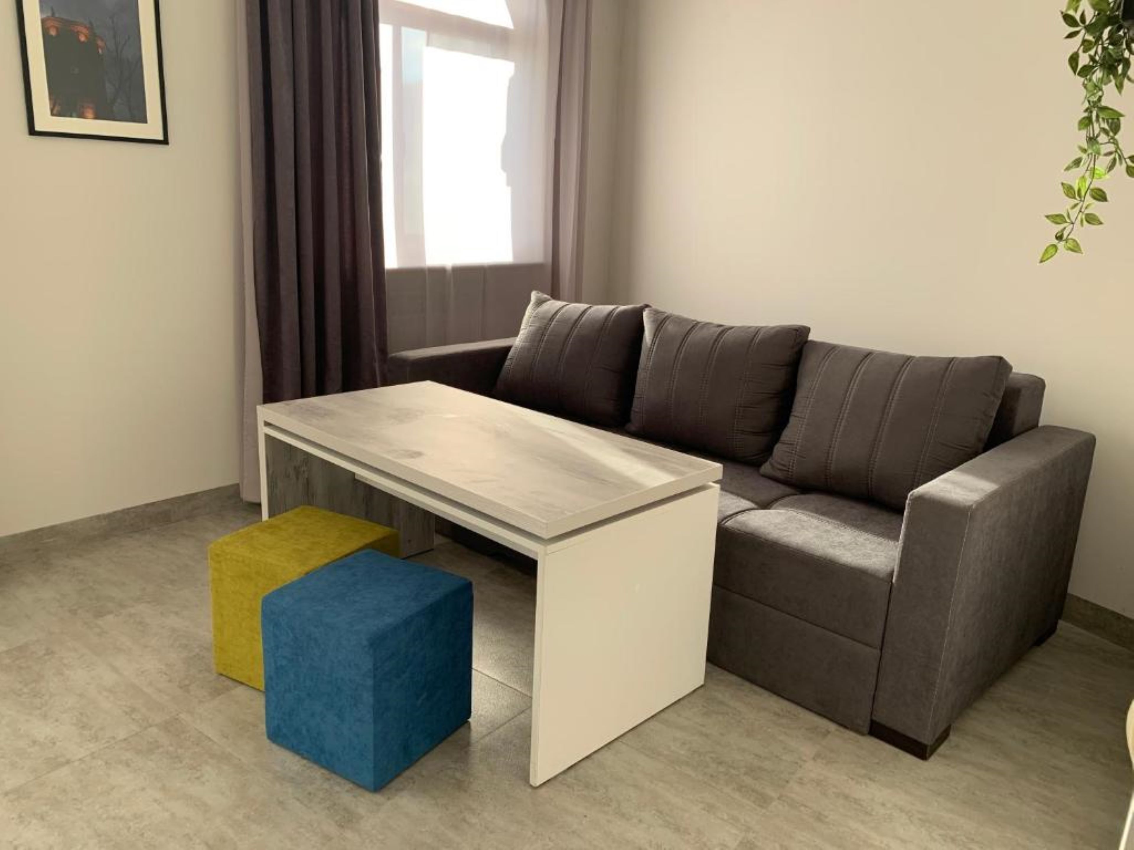 A modern living room with a grey sofa, a white coffee table, and two colorful ottomans.