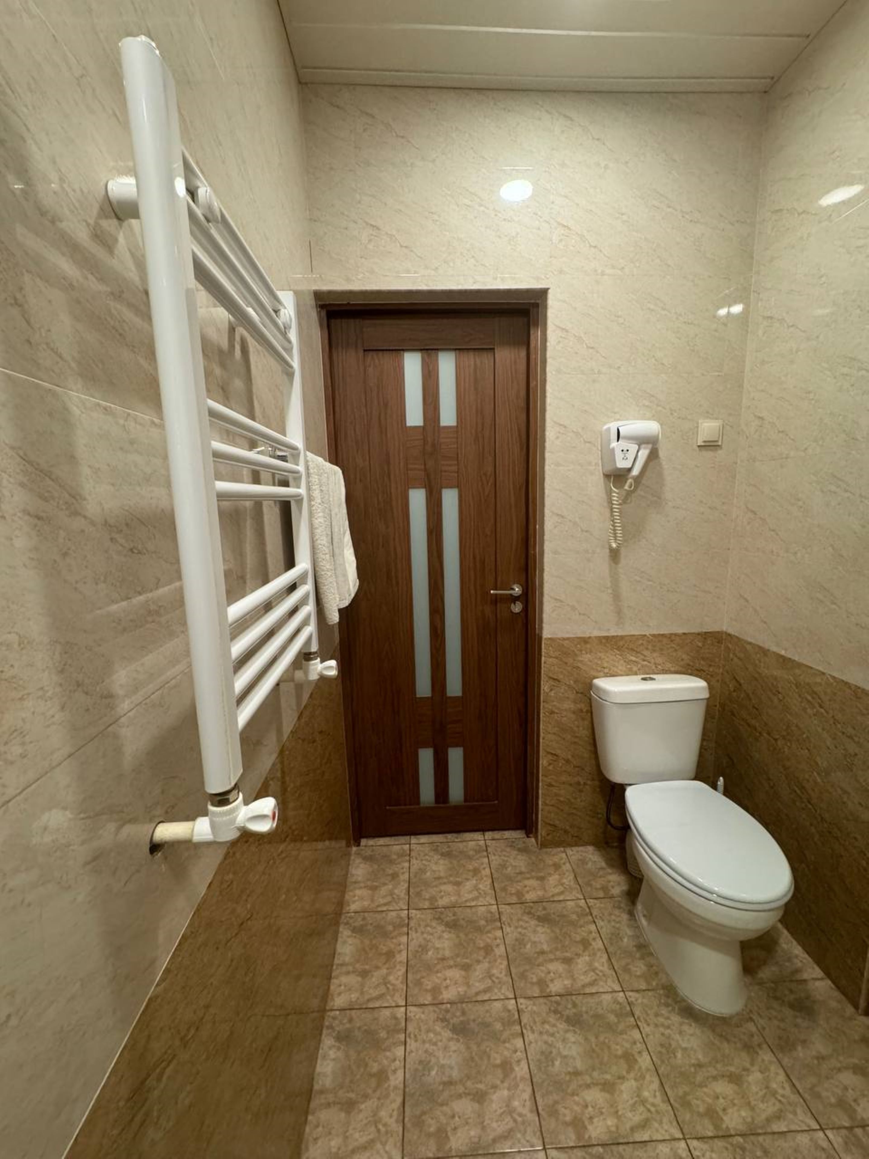 Un baño con inodoro, toallero, puerta y teléfono.